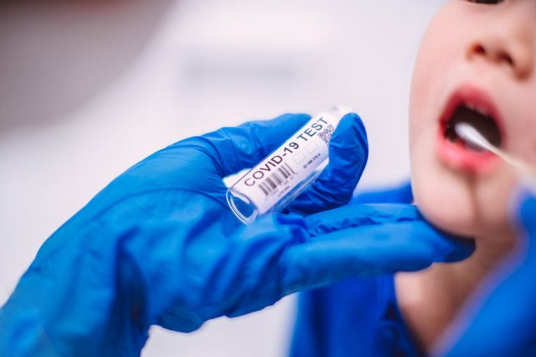 A doctor’s hands in protection gloves putting COVID-19 test swab into kid’s mouth