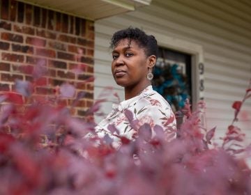 Tia Cunningham stands in front of home, with plant leaves in the foreground