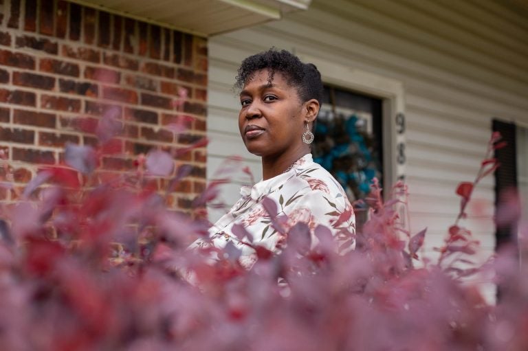 Tia Cunningham stands in front of home, with plant leaves in the foreground