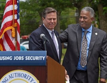 Interim Camden Mayor Vic Carstarphen, at right, who is running in the June 8 primary, shares a podium with US Rep. Donald Norcross, brother of South Jersey political power broker George Norcross, at a June 2 event to announce a $35 million grant to rebuild Ablett Village, a dilapidated Camden housing project. (Photo by April Saul for WHYY)