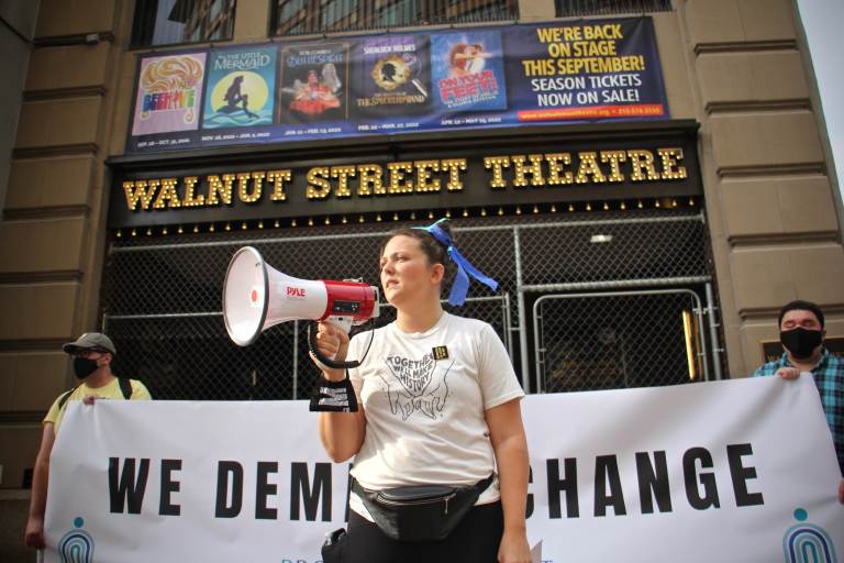 Organizer Jenna Pinchbeck reads the testimonies of those who suffered at the Walnut Street Theater to a crowd of about 80 protesters. (Emma Lee/WHYY)