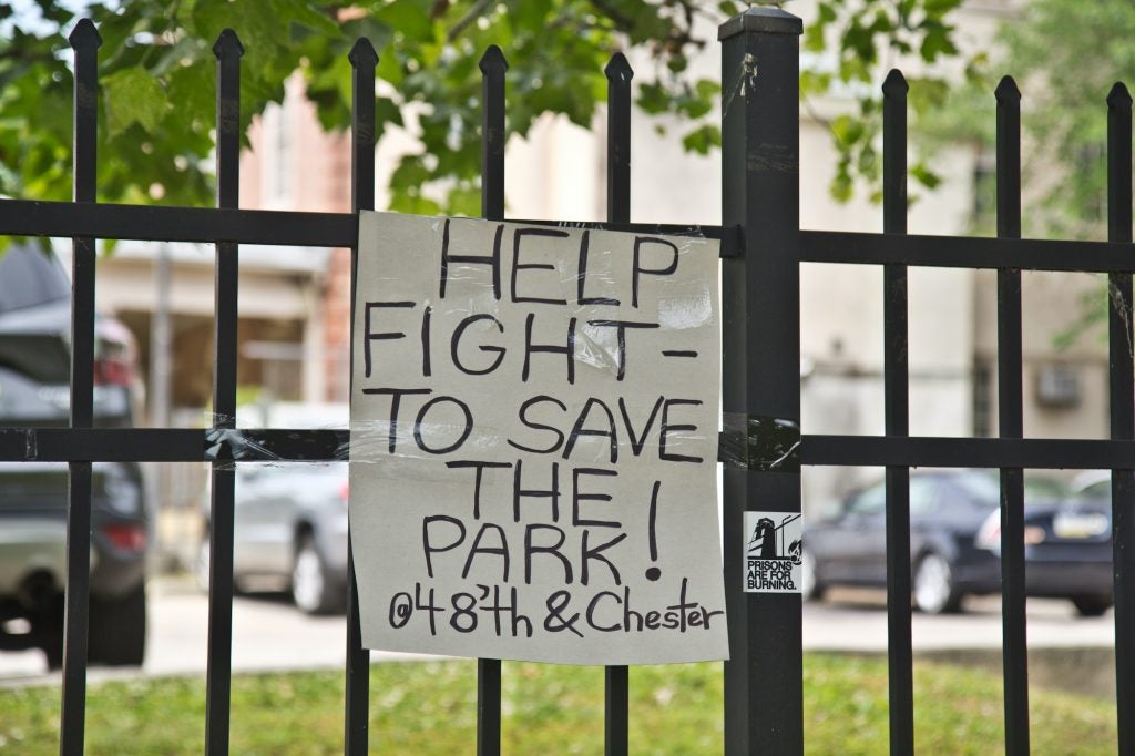 A sign on a fence reads, "Help fight to save the park @ 48th and Chester"