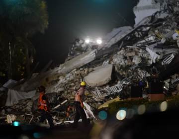 Rescue workers walk beside the rubble as rescue efforts continue