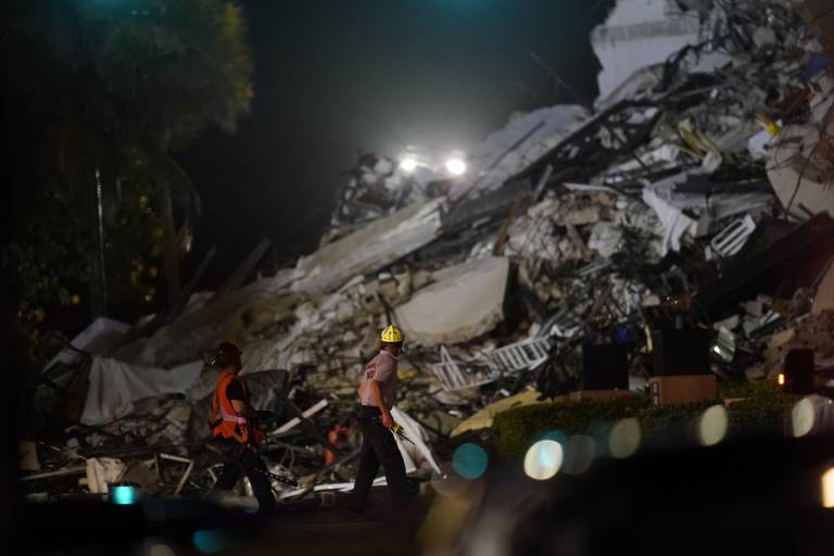 Rescue workers walk beside the rubble as rescue efforts continue