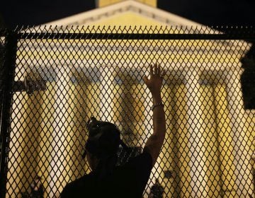 A protester calls out to police standing guard behind security fencing