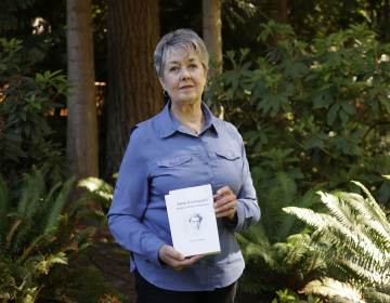 Karen McKnight stands in her backyard holding two books written by her brother