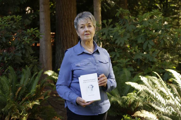Karen McKnight stands in her backyard holding two books written by her brother