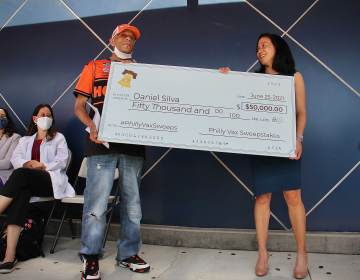 Vaccine sweepstakes winner Daniel Silva and Dr. Angela Duckworth hold a giant check during a press event at Maria de los Santos Health Center. (Emma Lee/WHYY)