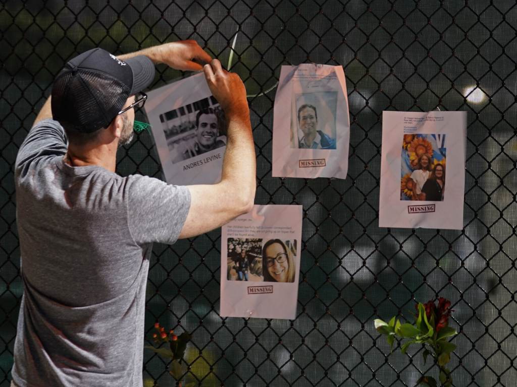 A man hangs a photo on a fence of someone missing near the site of an oceanfront condo building