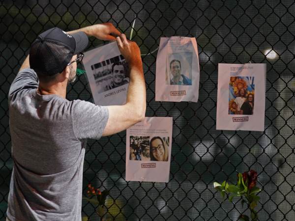 A man hangs a photo on a fence of someone missing near the site of an oceanfront condo building