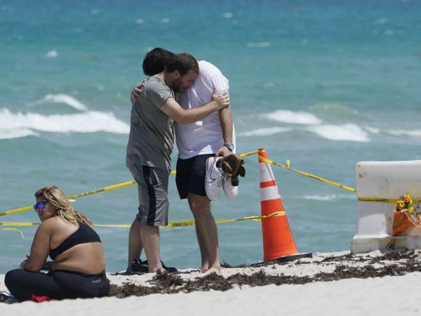 Two men console each other on the beach