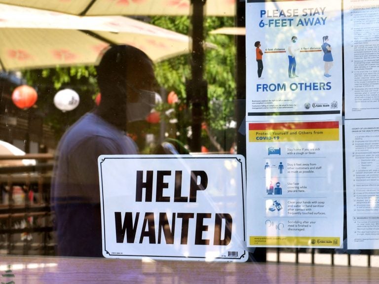 A 'Help Wanted' sign is posted beside coronavirus safety guidelines in front of a restaurant