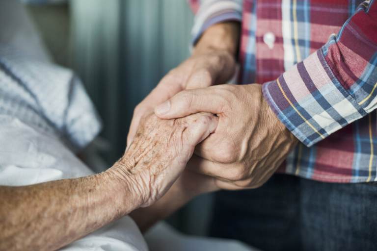 Close up of son holding his mothers hands in hospital