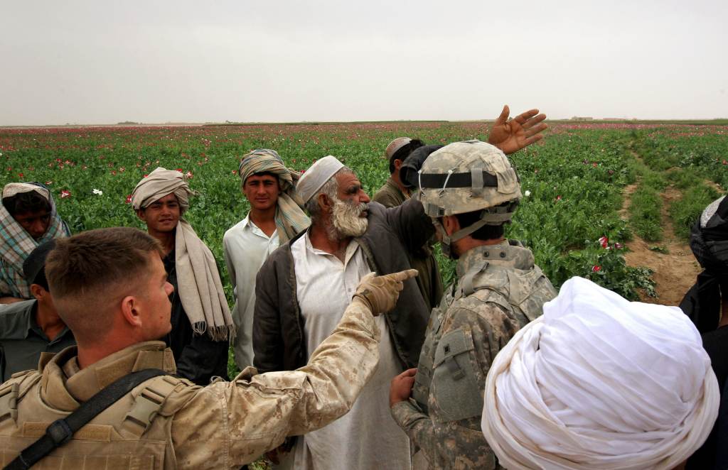 An opium farmer shows damaged poppies to U.S. Marines and their interpreter near Qalanderabad