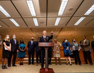 Gov. Tom Wolf speaks from a podium, flanked by other officials