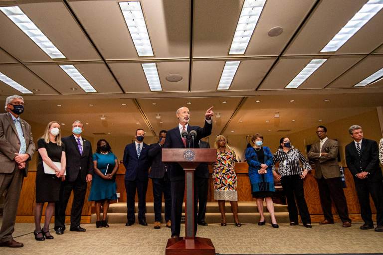 Gov. Tom Wolf speaks from a podium, flanked by other officials