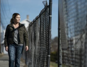 Kate Winslet, portraying her character Mare, walks along a fence