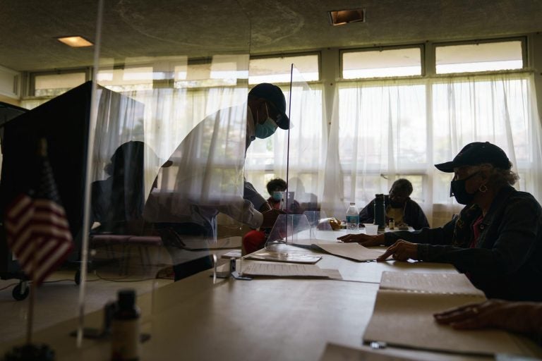 A voter signs in at a polling location, separated by a plastic partition