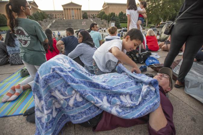 On Eakins Oval, a rambunctious Taaya Wittenmeyer, 9, covers his father, Brian Wittenmyer with a blanket during the family’s nearly 3 hour wait for the fireworks display at the Philadelphia Museum of Art. His family, from Ashburn VA was visiting Philadelphia over the Fourth of July weekend. (Jonathan Wilson for WHYY)