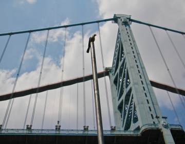 A tall pole is topped with a bronze bird as part of an art installation by the Ben Franklin Bridge