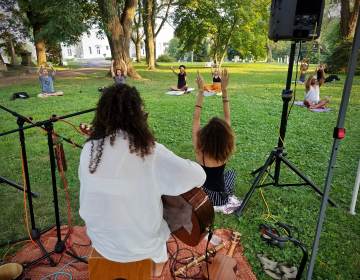 Aubrey Howard (in black tank) leads a session of intentional breathing meditation, accompanied by musician Alexia Oliveira, during a yoga session at the Woodlands cemetery. (Peter Crimmins/WHYY)