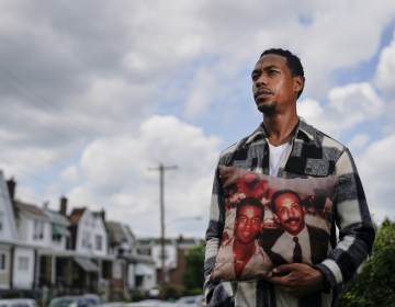 Brett Roman Williams poses for a photograph while holding a pillow with a photo of his father, Donald Williams, lower right, and brother Derrick Williams