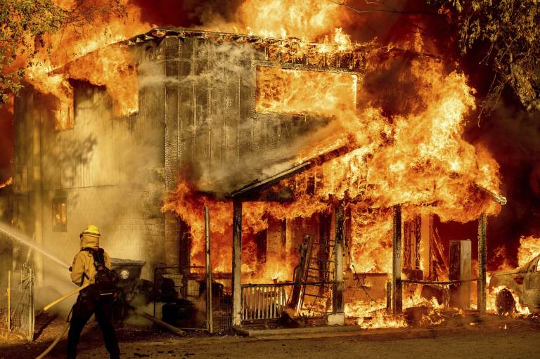 A firefighter sprays water while trying to stop the Sugar Fire from spreading to neighboring homes