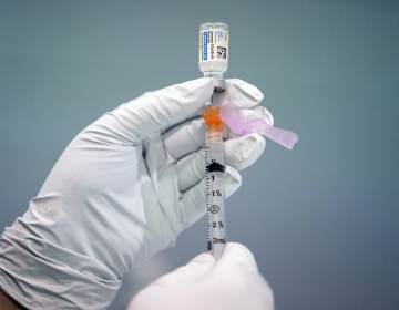 A gloved hand holds up a syringe of the COVID-19 vaccine