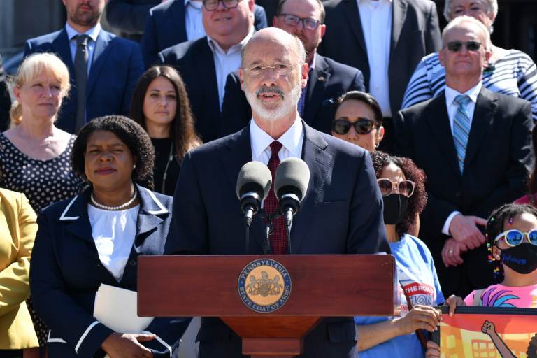 Gov. Tom Wolf speaks from a podium with people behind him