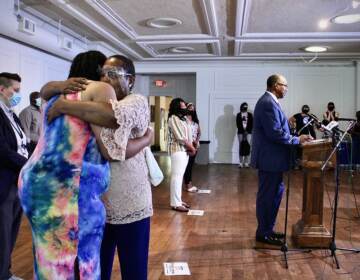 Rev. Andrea Harrington comforts Crystal Davis, with a speaker standing at a podium in the background