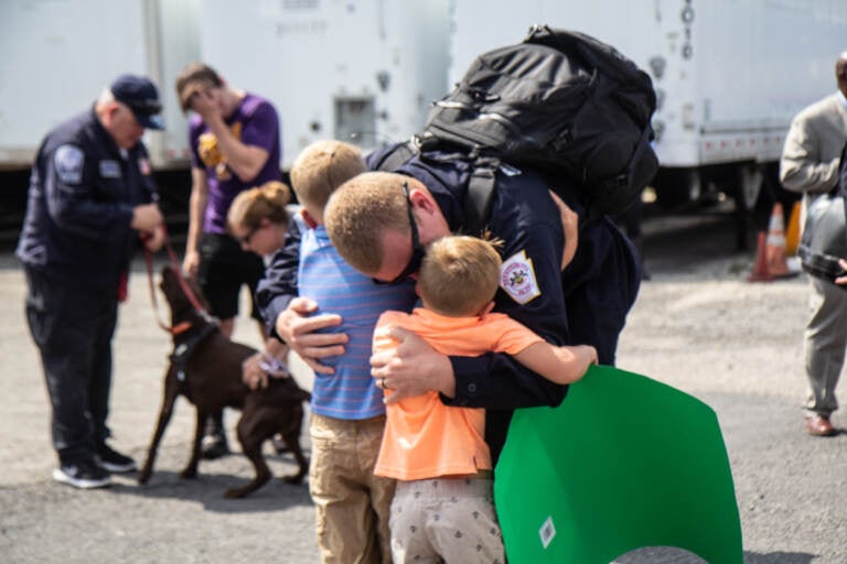 Brandon Watkins, a member of PA-Task Force 1, hugs his kids, Nicholas, 5, and Jackson, 7, in Philadelphia on July 16, 2021, after he returned from assisting in the search and recuse mission in Surfside City, Florida. (Kimberly Paynter/WHYY)