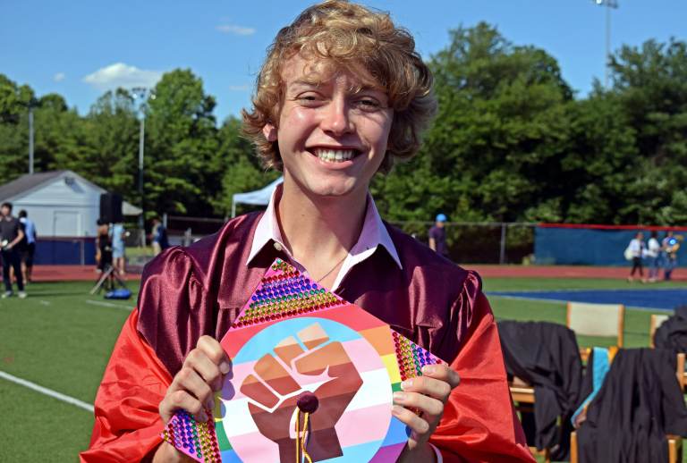 Bryce Dershem holds up his graduation cap, which features a fist on top of a trans pride flag