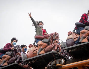 Park patrons ride the Pony Express roller coaster ride, one pictured in center wearing a mask and throwing up a peace sign