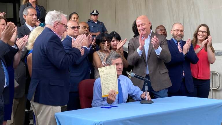 Delaware Gov. John Carney holds a newly signed copy of SB 15, with onlookers behind him