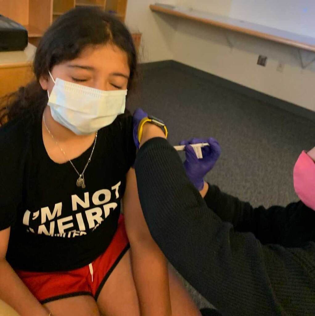 Maya Huber receives a COVID-19 vaccine while wearing a face mask and closing her eyes