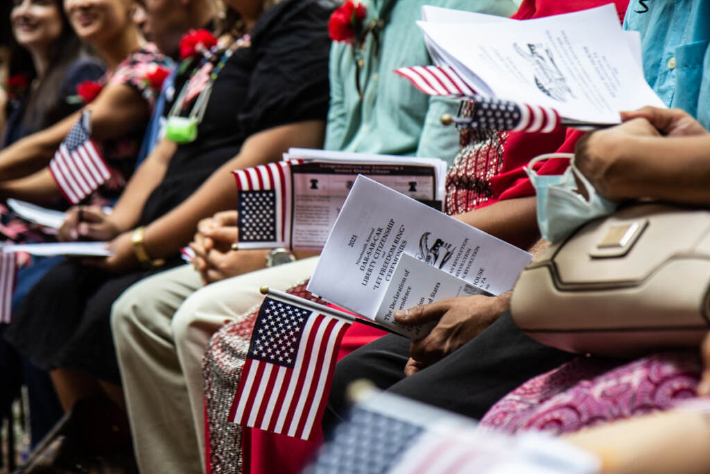 People hold American flags and papers during a naturalization ceremony