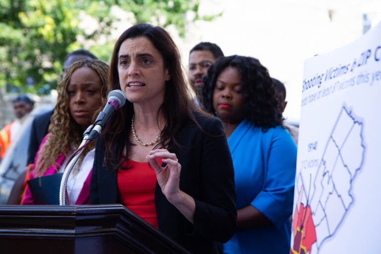 Rebecca Rhynhart speaks from a podium at a press conference, with elected officials behind her