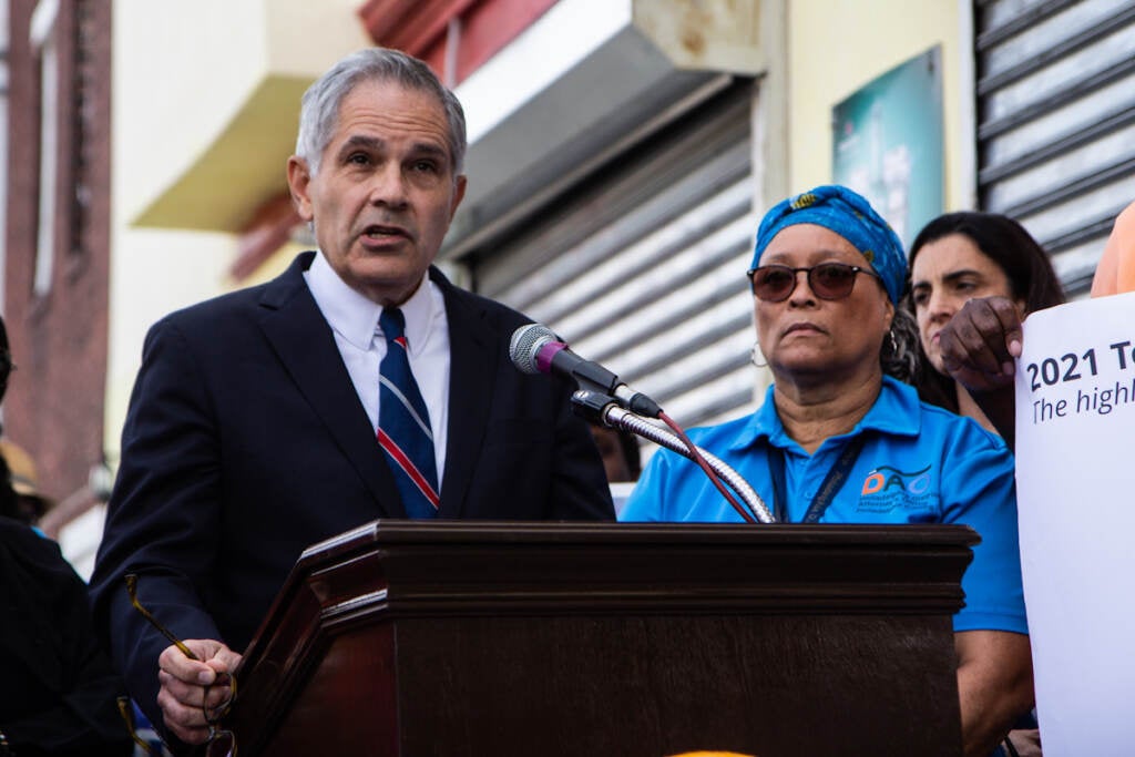 Larry Krasner speaks from a podium at a press conference, with elected officials behind him