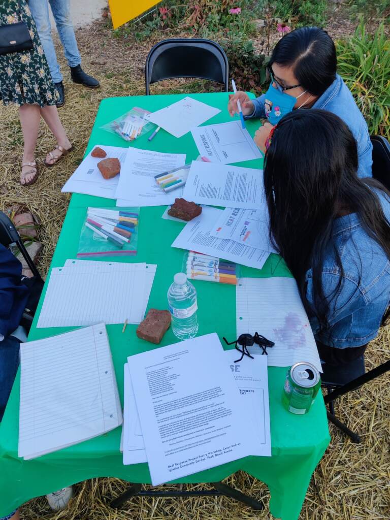 Two people sit at a table with coloring book supplies