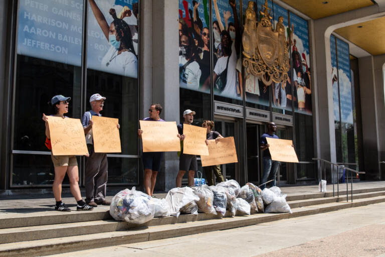 Protesters hold signs in front of bags of trash on the steps of the MSB