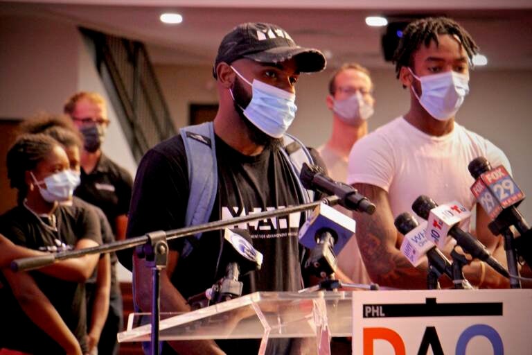 James Aye, wearing a mask, speaks at a DAO press conference