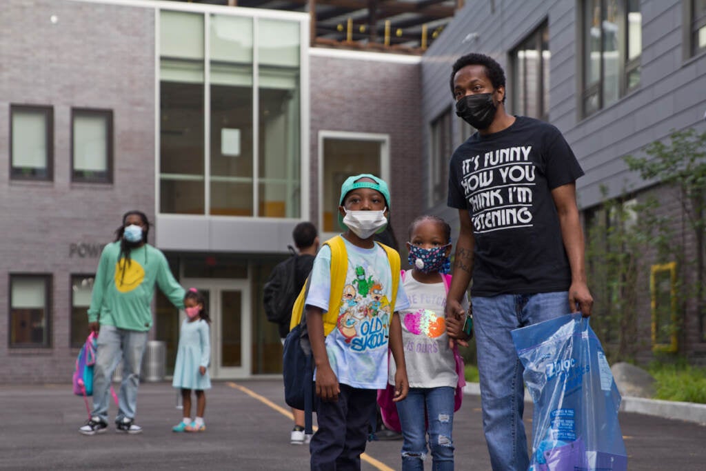 A family poses for a photo while wearing face masks outside their school