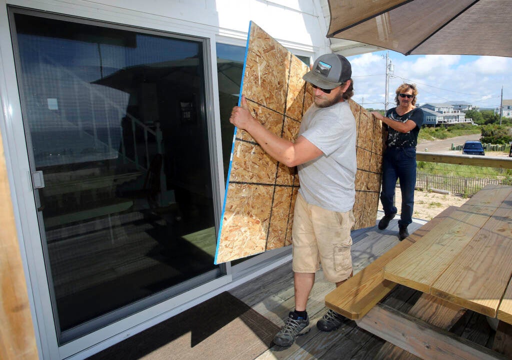 James Masog (center) and Gary Tavares move particle board into place to board up the sliding glass doors of a clients house in Charlestown, R.I., ahead of Hurricane Henri