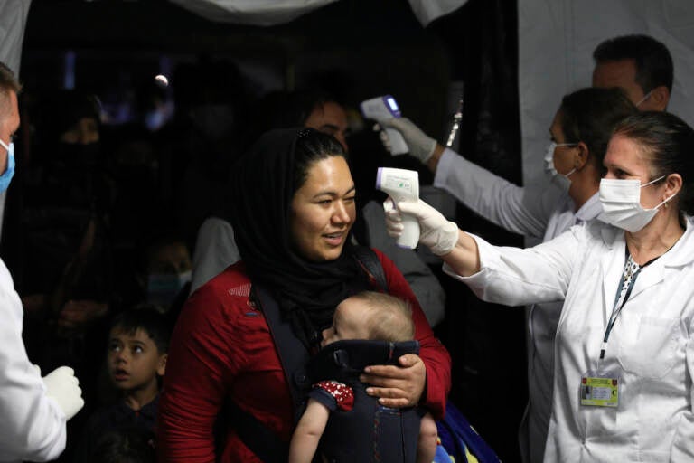 Health workers checks the temperature of evacuated citizens from Afghanistan upon their arrival at Tirana International Airport in Tirana, Albania, Friday, Aug. 27, 2021. A government decision has planned that the Afghans may stay at least a year during which they will proceed with their application for special visas before they move on to the US for final settlement. (AP Photo/Franc Zhurda)