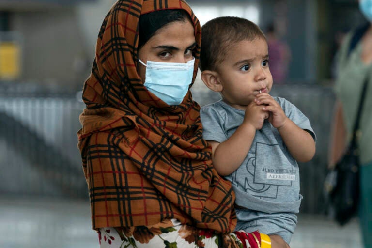 An Afghan woman wearing a face mask holds a child