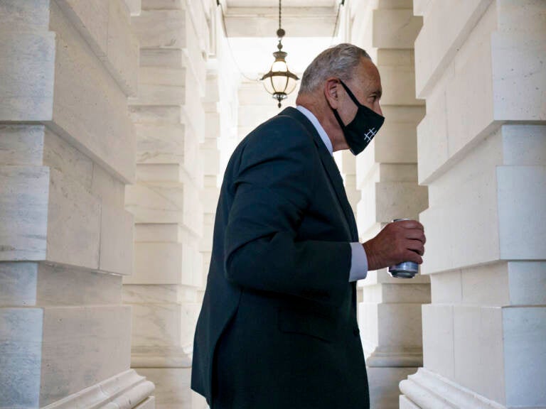 Chuck Schumer walks while carrying a beverage and wearing a mask