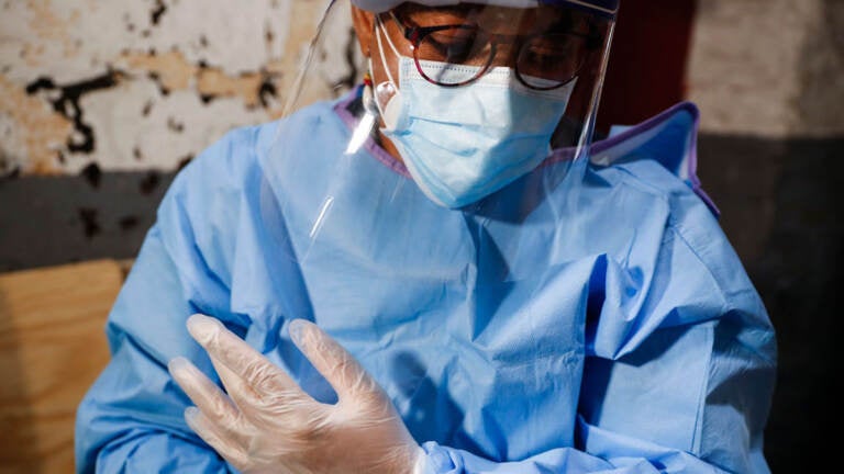 A closeup of a health worker wearing a face mask, scrubs, and gloves