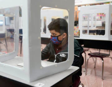 Julian Aldridge wears a face mask while sitting at a desk behind a see-through partition