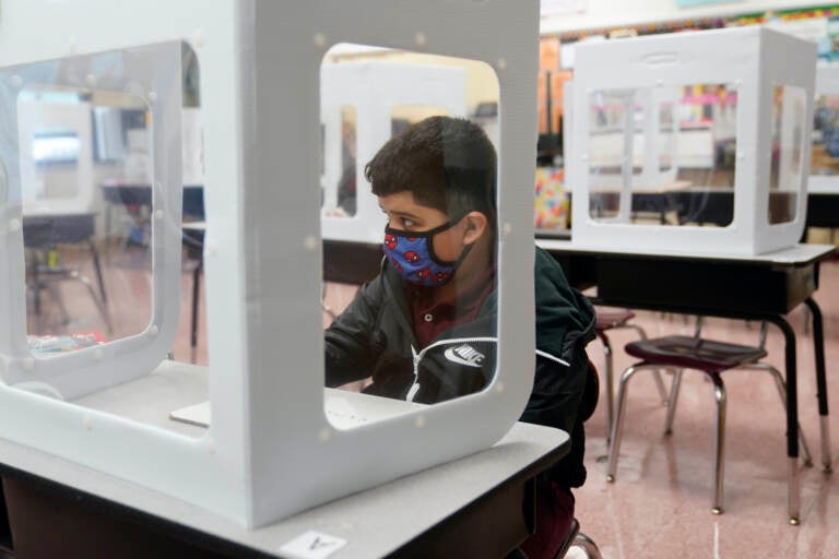 Julian Aldridge wears a face mask while sitting at a desk behind a see-through partition