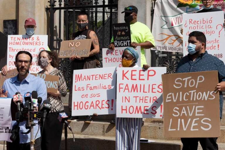 People from a coalition of housing justice groups hold signs protesting evictions during a news conference